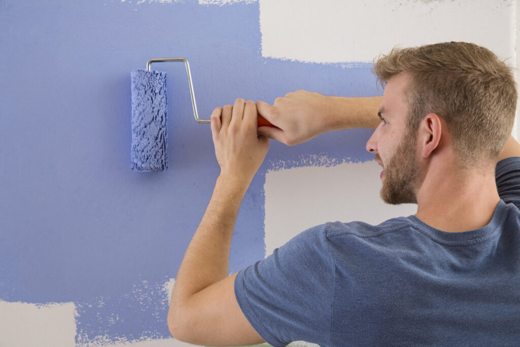 Mann streicht Wand mit AURO Wandfarbe im blauvioletten Farbton 50.7 cornflower